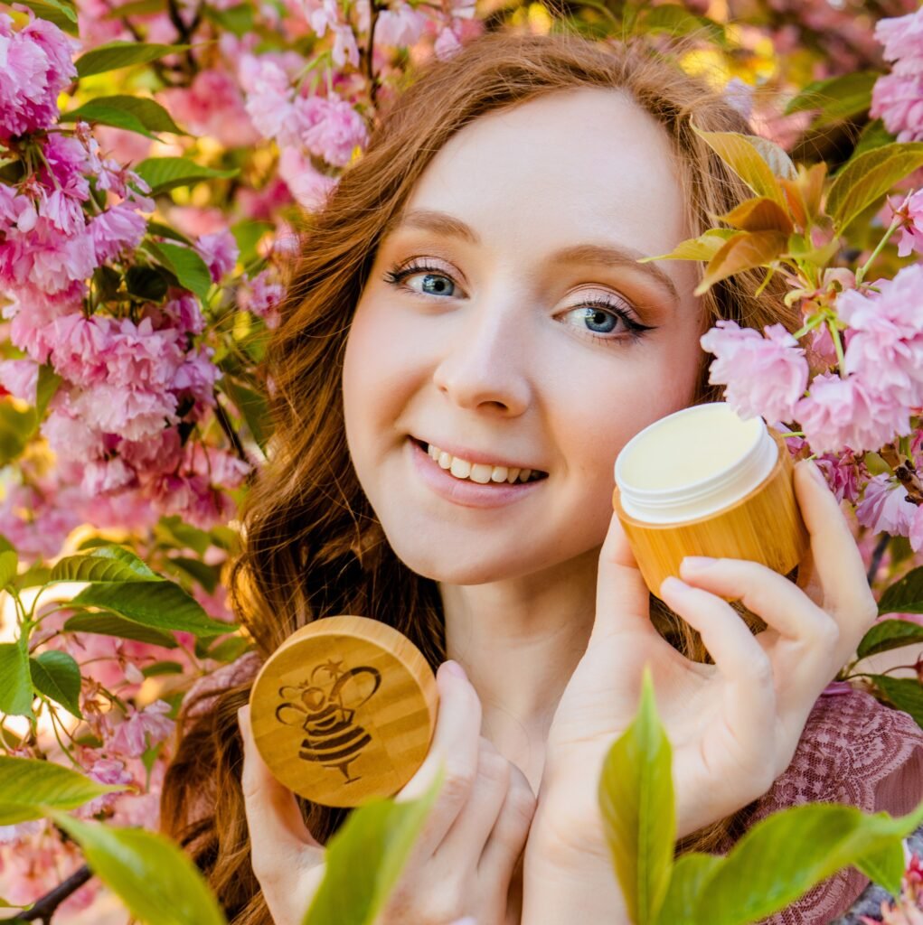 “Woman holding The Bee Fairy natural beeswax skin balm in a bamboo pot surrounded by spring blossom — handcrafted natural skincare from the Teme Valley.”