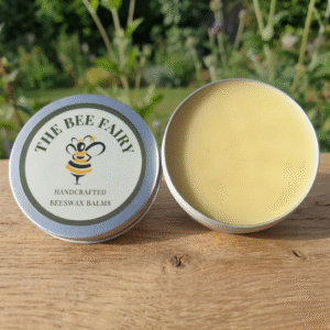 The Bee Fairy Everyday Hand Balm in aluminium tin, open to show natural beeswax balm on wooden surface with soft garden background